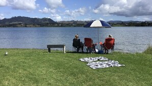 Un cadre agréable au bord du lac, avec une pelouse, un banc et une table entourée de chaises, le tout à l’ombre d’un parasol de plage.