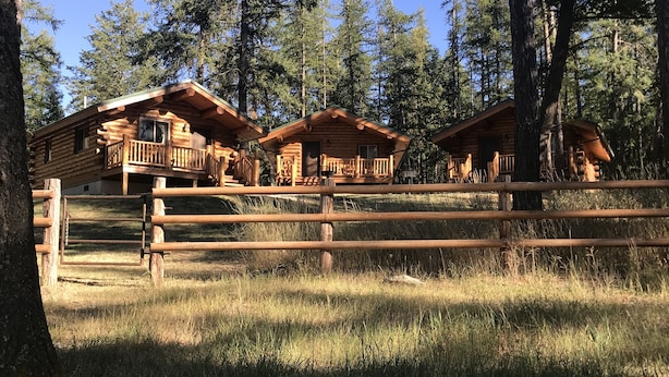 Eine Holzhütte mit Balkon, umgeben von hohen Bäumen und einem Holzzaun.