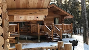 Eine Blockhütte mit einer Holzdachterrasse und einer Treppe, die zu einem Balkon führt.