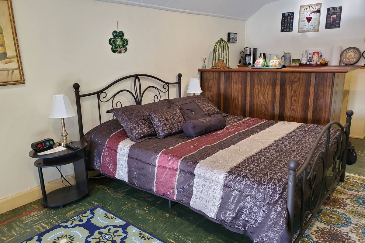 A neatly arranged bedroom with a bed, bedside tables, a nightstand, a wooden dresser, and a patterned rug.