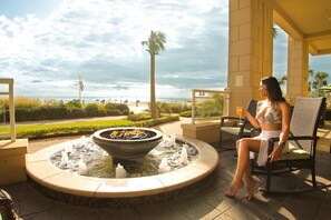 Una mujer sentada junto a una fogata con vista a la playa y al océano.