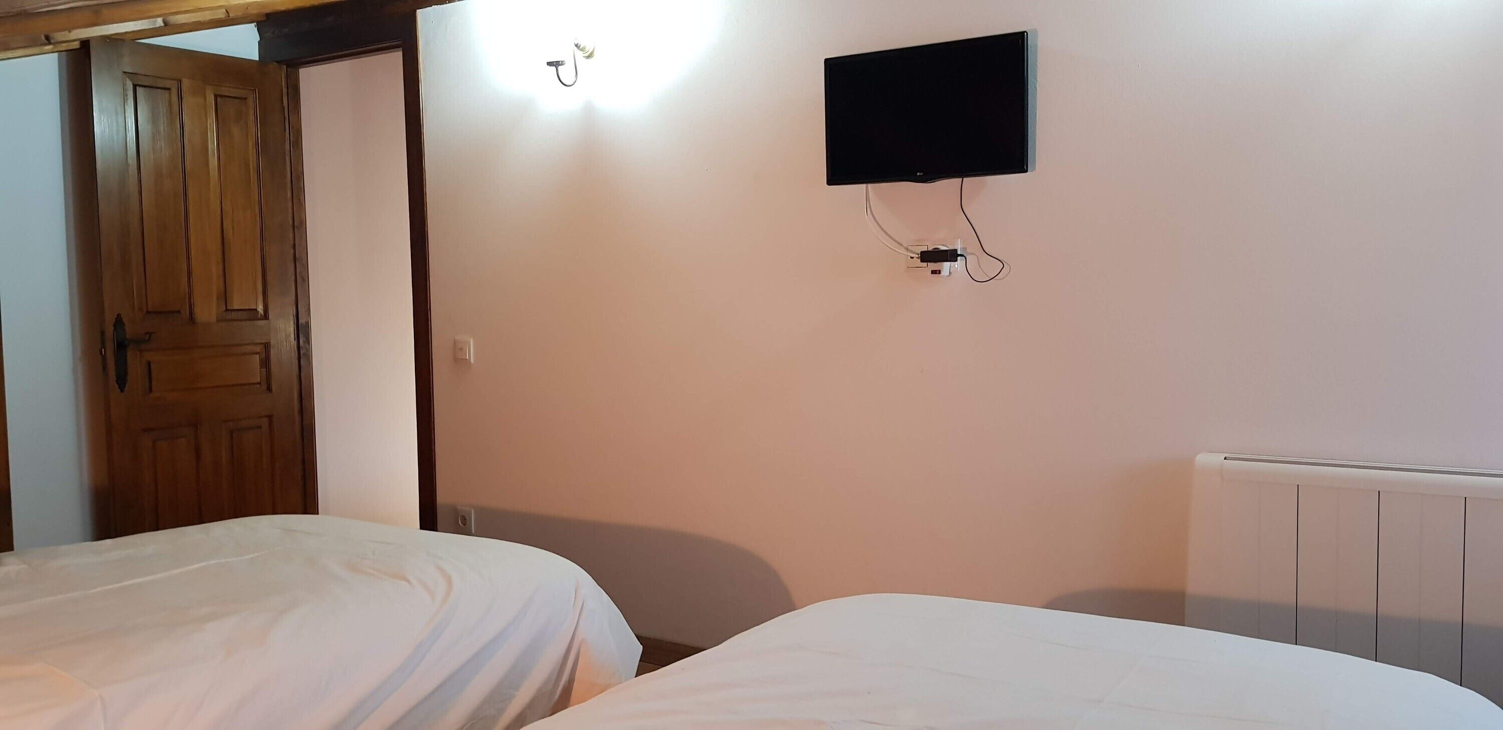 A room with two beds, a wooden door, a wall-mounted TV, and a radiator.