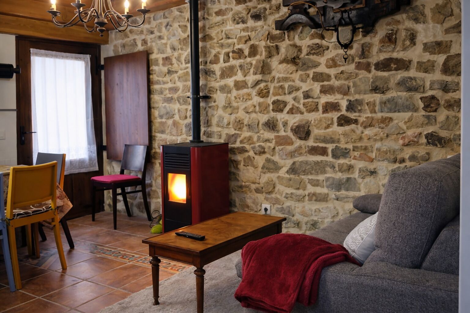 A cozy living room with a stone wall, a wooden table, a red blanket, and a sofa.