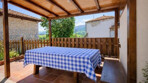 A covered patio with a checkered table and benches, stone walls, and a view of the countryside. - La Casina de Marina de Tresgrandas (Llanes) (Tresgrandas)