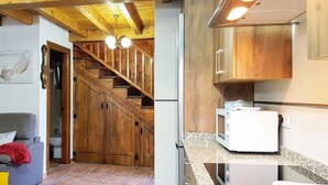 A living room with a sofa, a red pillow, and a painting of butterflies. A wooden staircase leads to a kitchen with wooden cabinets and a white refrigerator. - La Casina de Marina de Tresgrandas (Llanes) (Tresgrandas)