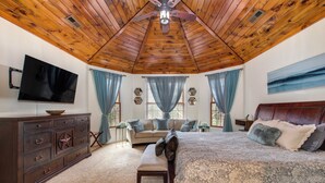 Een slaapkamer met een houten plafond, een groot bed, een dressoir, een televisie en een raam met gordijnen.