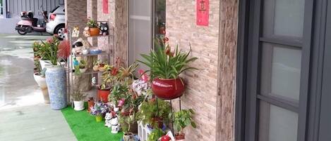 A building entrance with a red banner, potted plants, and a scooter parked outside.