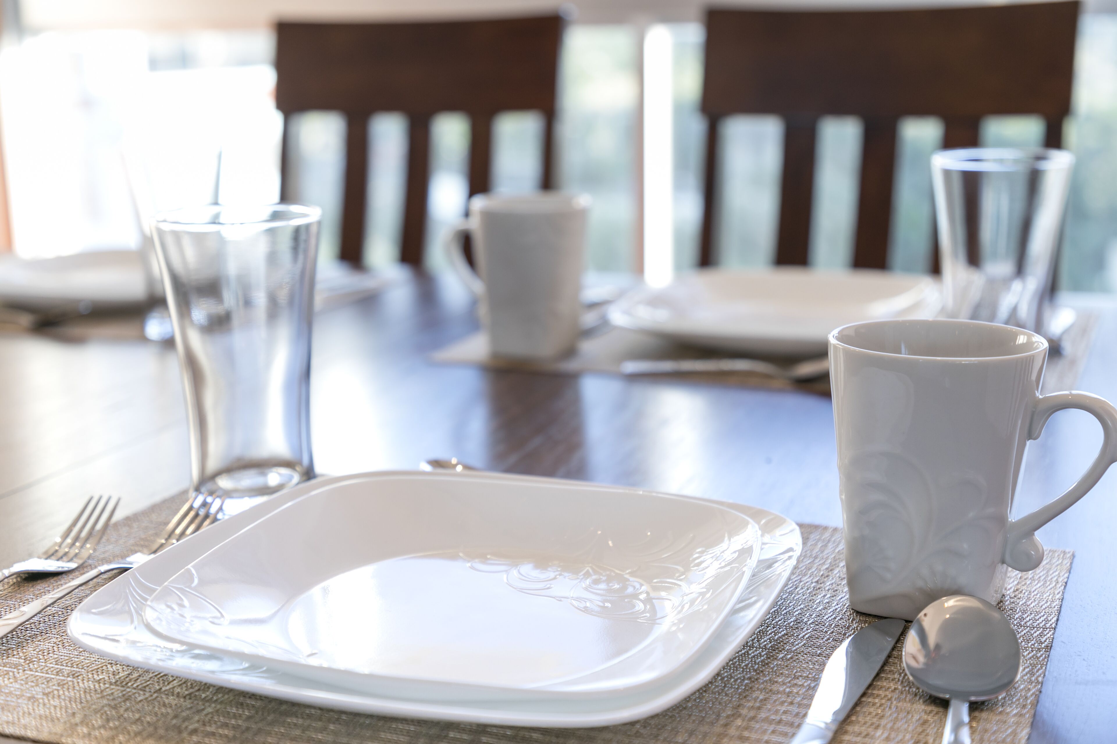 A dining table set with white plates, a white mug, and clear glasses.