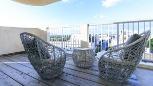 Un balcon avec des fauteuils en osier et une petite table, donnant sur un paysage urbain.