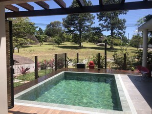 A clear pool with a wooden deck, surrounded by a metal fence and a grassy area with trees and a red fire hydrant. - Contemporary house near the beach with heated pool, hot tub and barbecue (Campeche Leste)