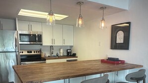 A modern kitchen with a wooden island, bar stools, stainless steel appliances, pendant lighting, and a framed artwork on the wall. - One block to Vanderbilt Beach! (Naples)