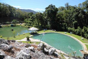 A swimming pool surrounded by lush greenery, with a small pavilion and lounge chairs.