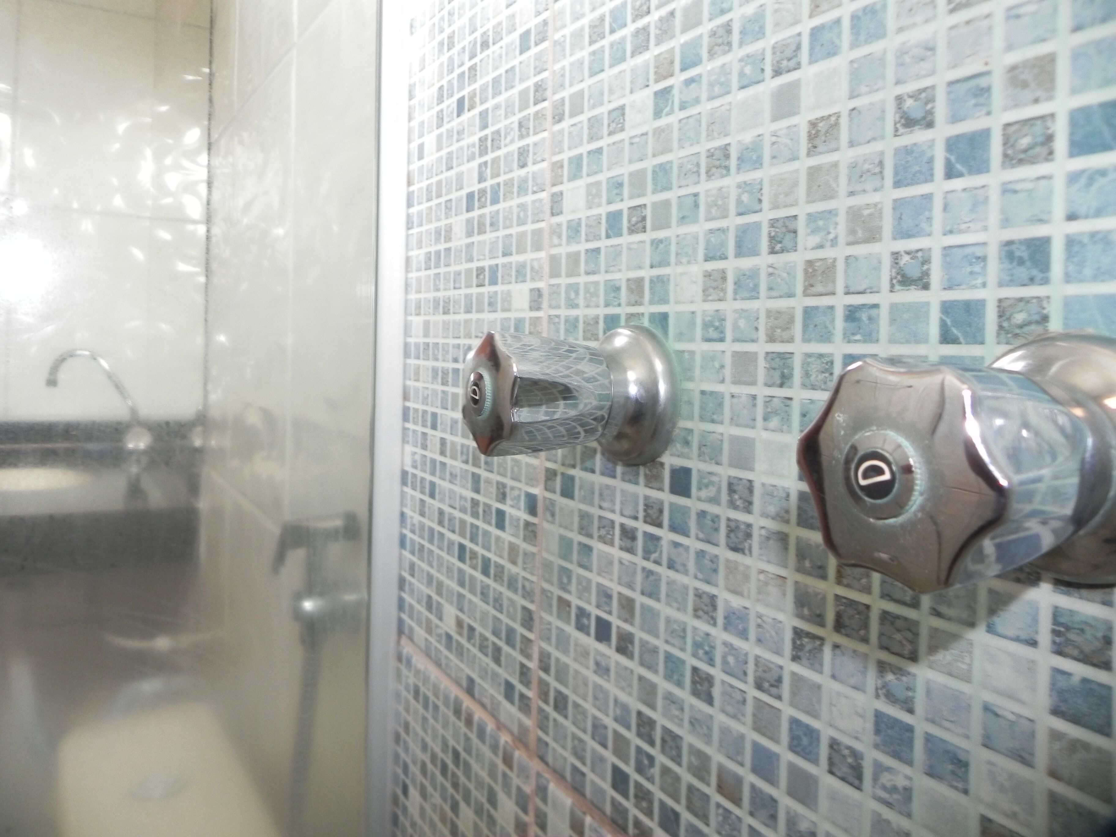 A bathroom with a tiled wall, a shower door, and a faucet.