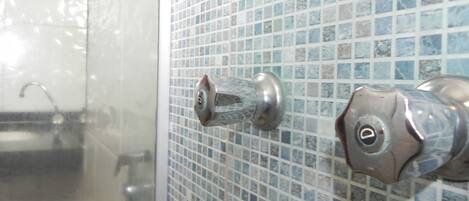 A bathroom with a tiled wall, a shower door, and a faucet.