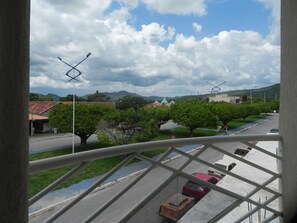 A view from a window overlooking a street with parked cars, trees, and a distant mountain range. - Planeta Hotel (Colinas do Sul)