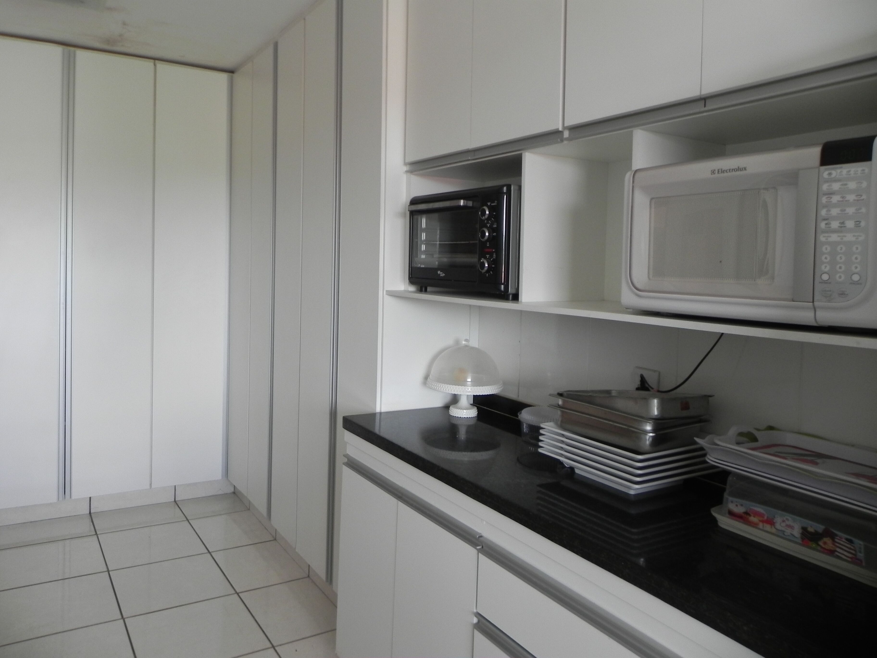 Een keuken met witte kasten, een zwart aanrecht, een magnetron, een oven en een taartrooster met een taart.