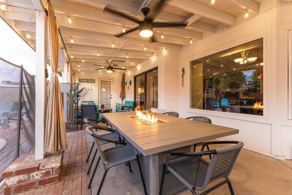 Un espacio de comedor al aire libre con una mesa larga, sillas, un ventilador de techo y una chimenea.