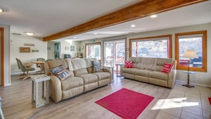 Un salón amplio con dos sofás color beige, techo de madera y grandes ventanales con vistas al exterior.