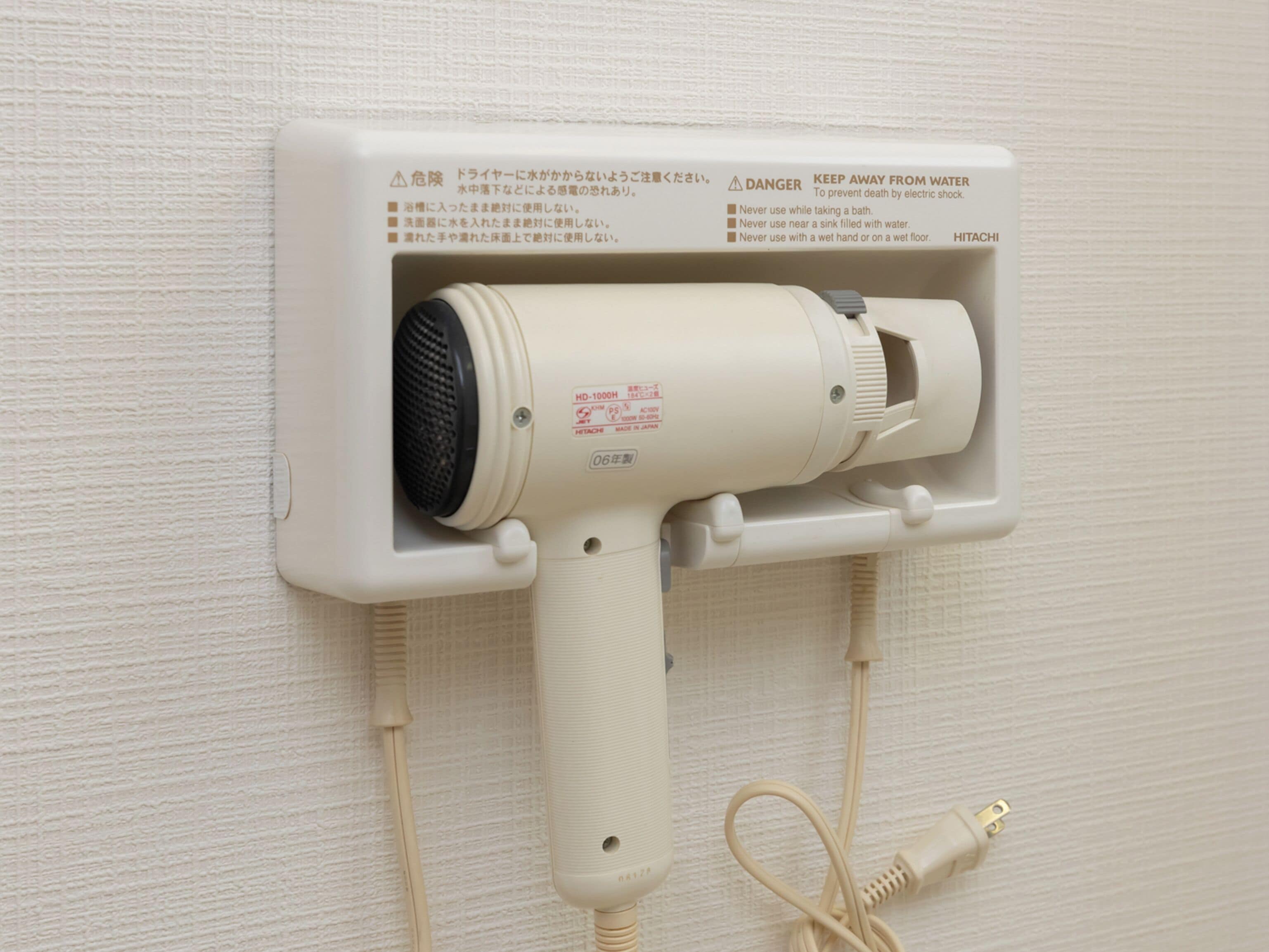 Un secador de pelo fijado a la pared, con instrucciones de seguridad y un cable de alimentación.