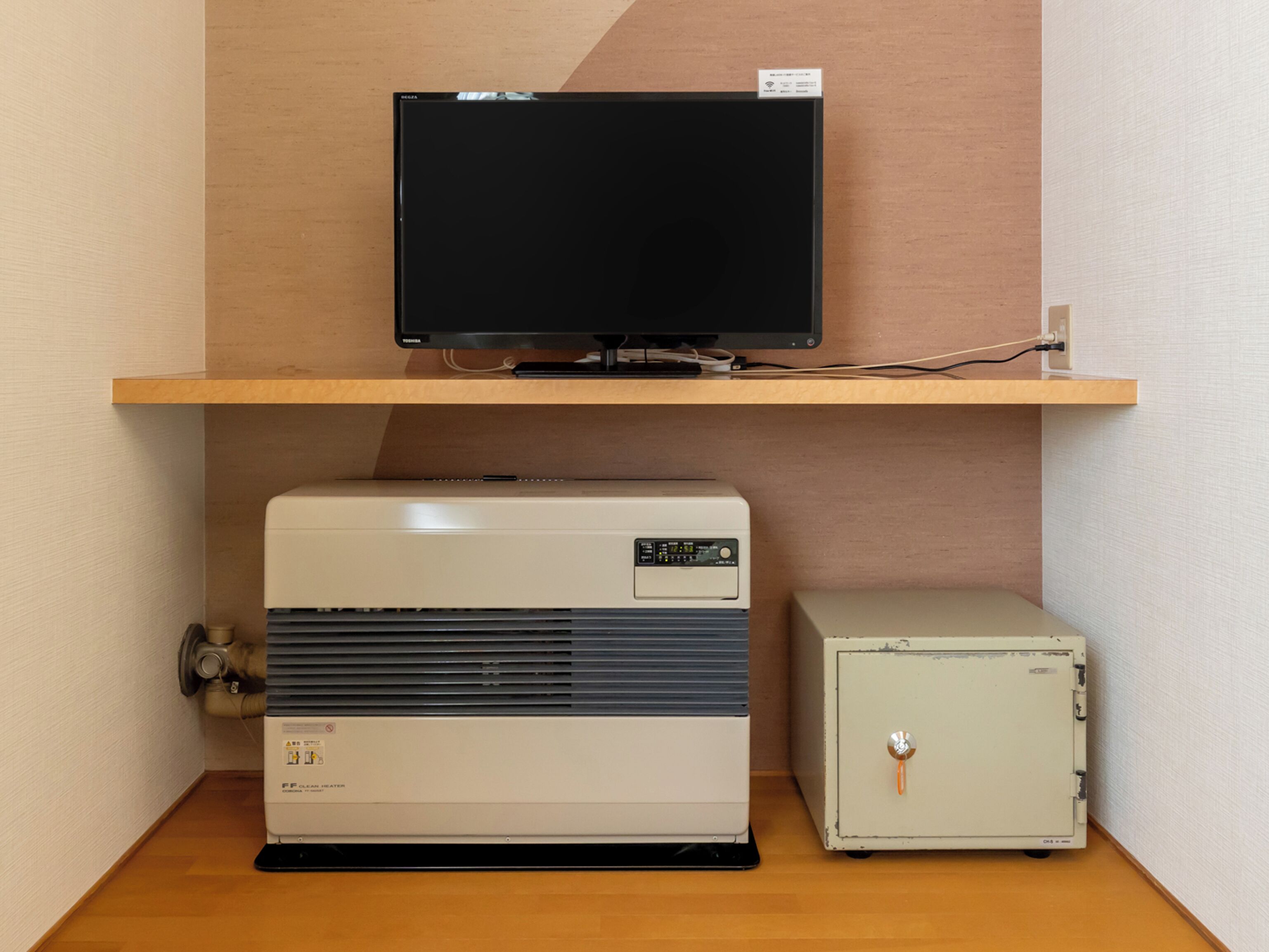 Una habitación con una televisión en un estante de madera, un aire acondicionado blanco y una caja fuerte pequeña y blanca.