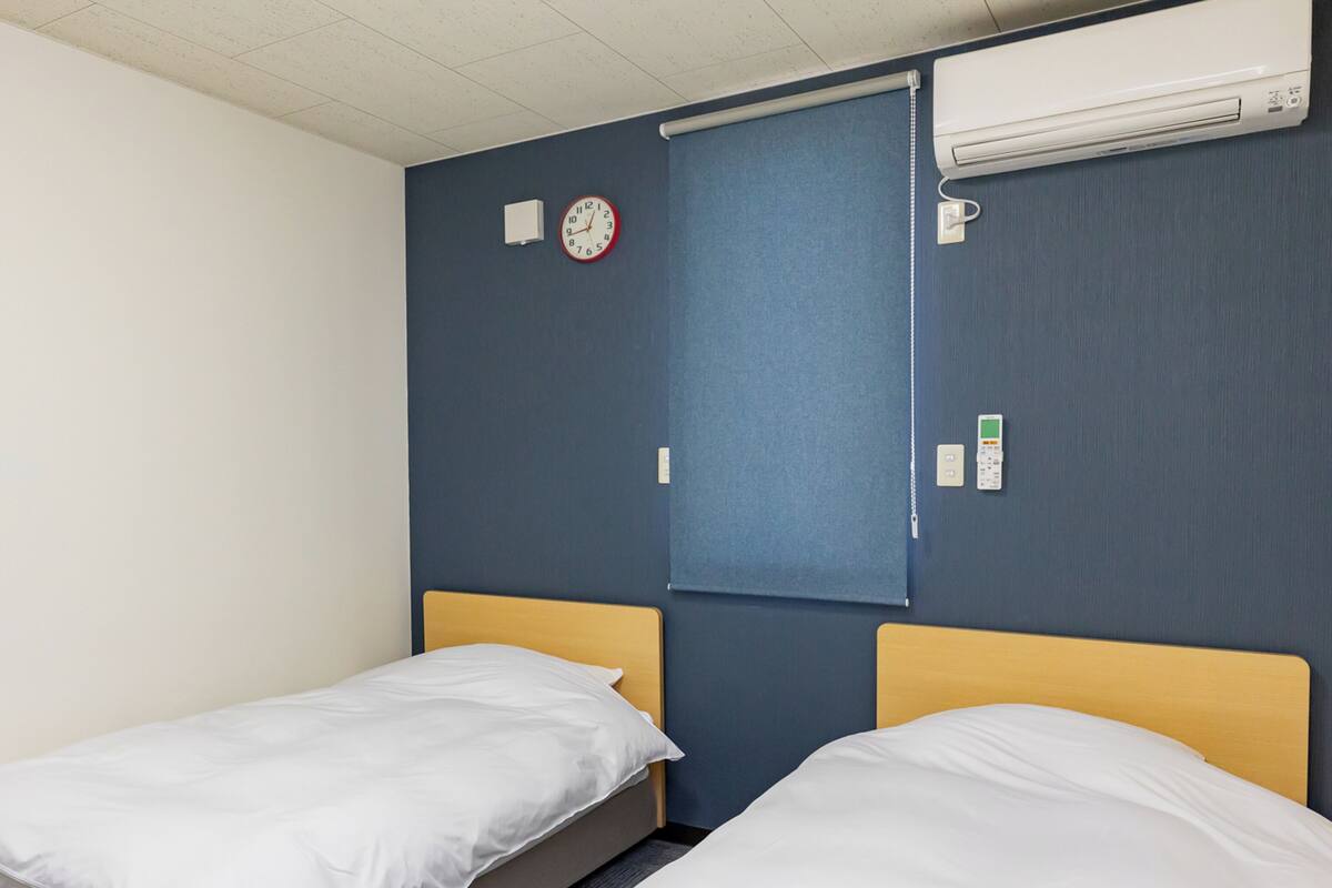 Ein Hotelzimmer mit zwei Einzelbetten, einer Wanduhr, einer Klimaanlage und einer Steckdose.