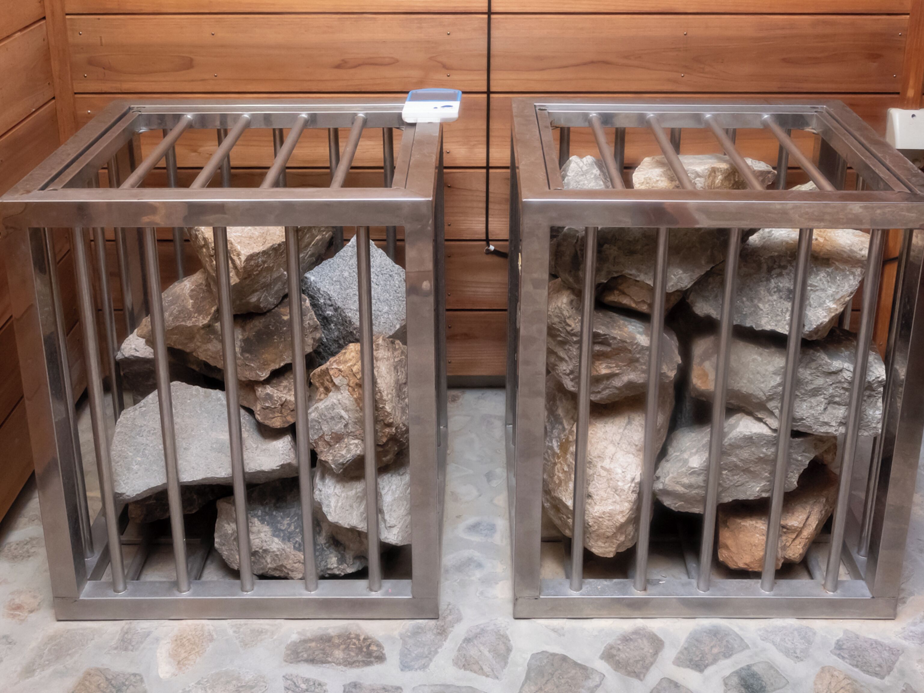 Two metal cages with rocks inside, placed on a stone floor.