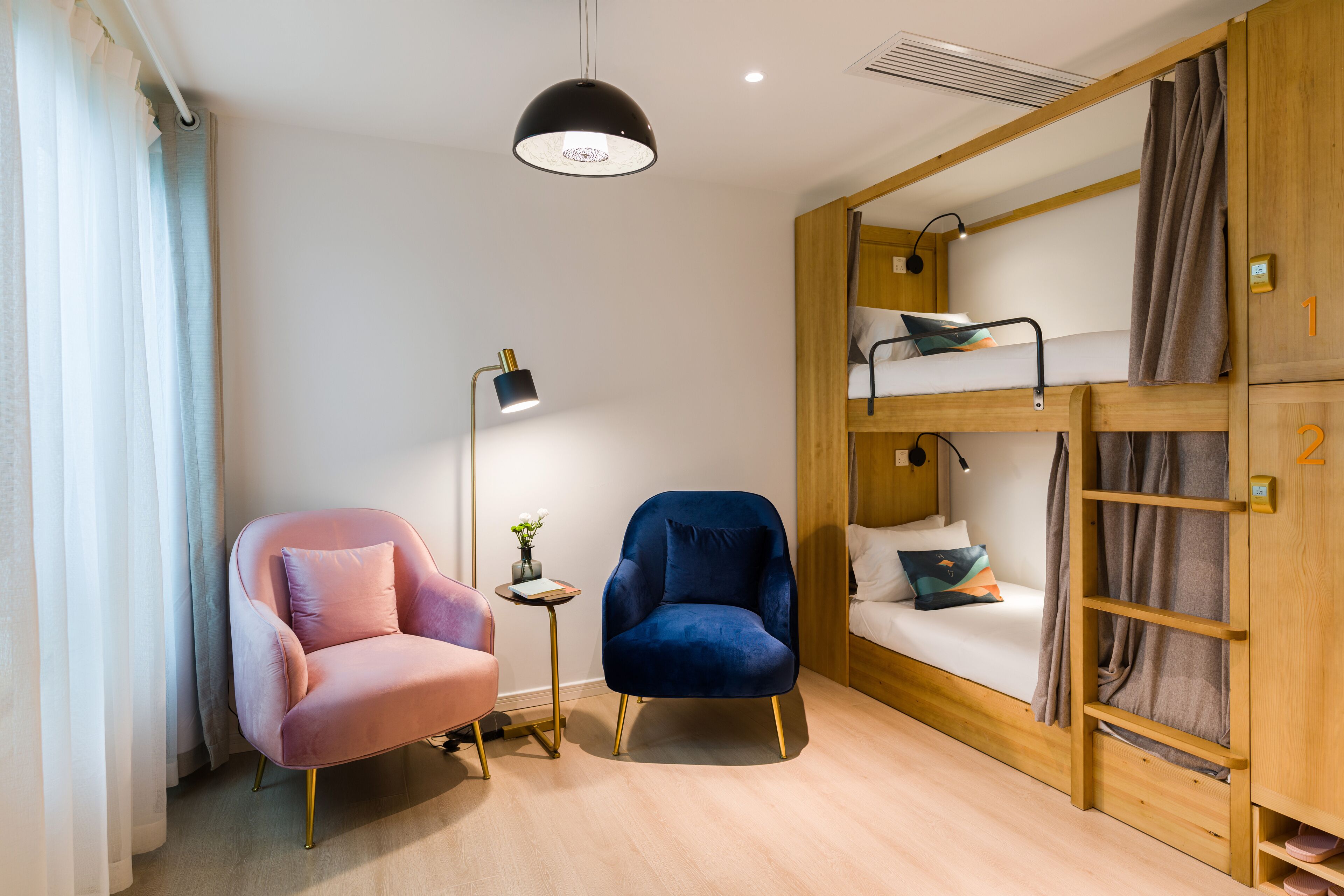 Ein Zimmer mit einem Etagenbett, einem rosa Stuhl, einem blauen Stuhl, einem kleinen Tisch mit Lampe und einer Deckenleuchte.