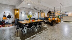A spacious room with a long wooden table, black chairs, a sofa, and a coffee table. There is a small stage with musical instruments and a drum set. - Hexi Boutique Hotel Chengdu (Chengdu)