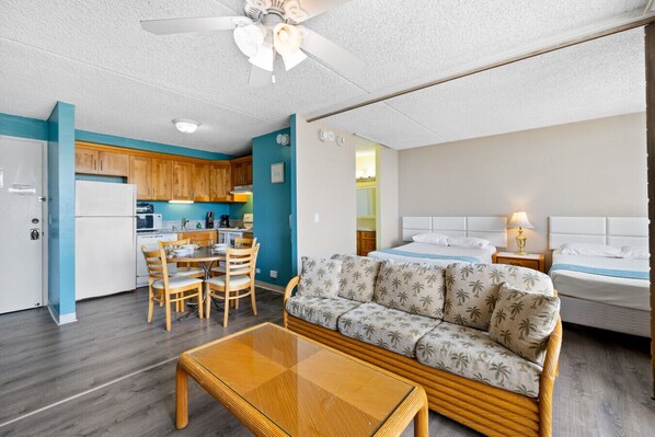 A compact hotel room with a kitchenette, a sofa, a bed, and a dining area.