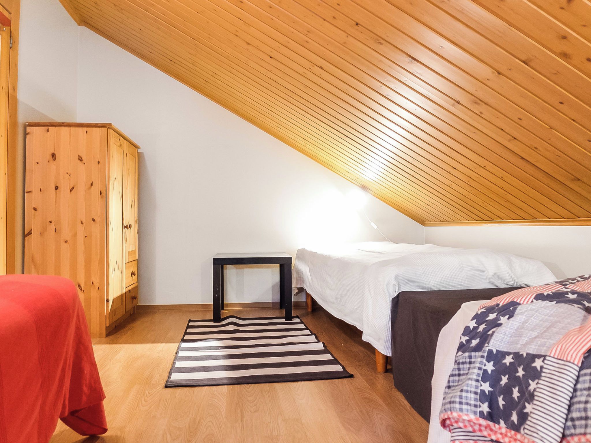 Een slaapkamer met een schuine kap, een houten garderobe, nachtkastjes en een gestreept tapijt.