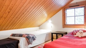 A bedroom with a sloped ceiling, a bed with a red blanket, a bedside table, and a window with a view of trees. - Rome 10 by Interhome (Pudasjärvi)