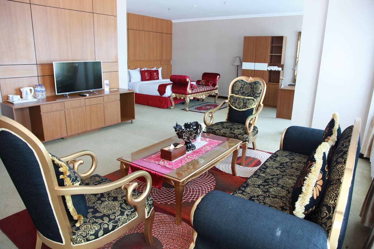 A hotel room with a bed, a TV, a desk, and seating area with chairs and a sofa.