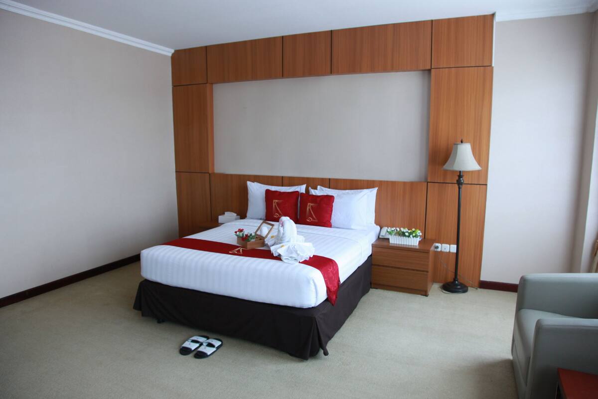 A hotel room with a large bed, wooden headboard, bedside tables, a lamp, and a chair.