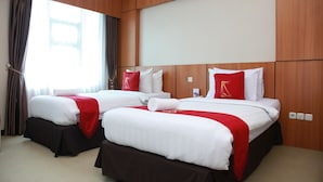 Habitación de hotel con dos camas, cada una con ropa de cama blanca y detalles rojos, paneles de madera en las paredes y un ventanal con cortinas.