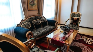 Una habitación tradicional con un sofá, un sillón a juego, una mesita de centro de vidrio y una alfombra estampada.