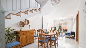 Un vaste espace dédié à la salle à manger, avec des chaises en bois et une table centrale, un escalier avec des rampes en bois, et une vue sur le salon.