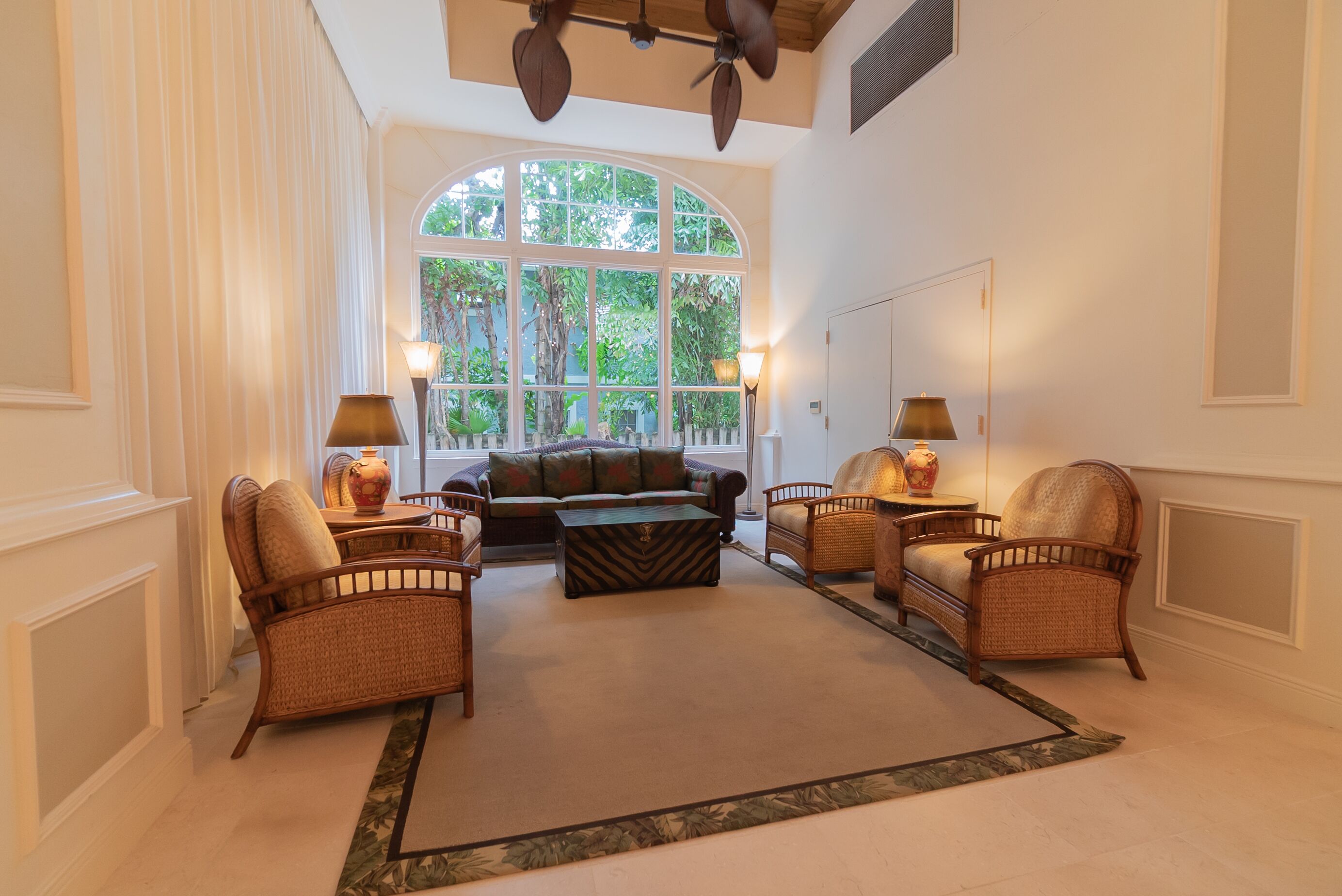 A spacious living room with a large arched window, a sofa, two armchairs, a coffee table, and two floor lamps.