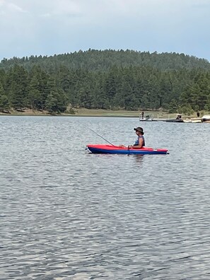 A person in a red kayak on a calm lake with a forested hill in the background. - Cozy & Comfortable Cabin in The Pinetop White Mountains - LONG TERM SPECIAL (Pinetop)
