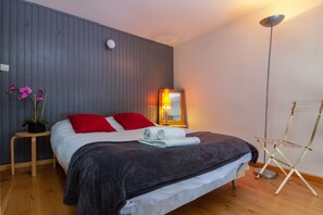 A neatly made bed with red and white pillows, a bedside lamp, and a small table with a potted plant. - Grand Roc C314 280m from Slopes, View, Parking & WiFi, Argentière (Chamonix), France (Argentière (Chamonix))