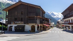 A wooden building with a café sign, a street with crosswalks, and snow-capped mountains in the background. - Grand Roc C314 280m from Slopes, View, Parking & WiFi, Argentière (Chamonix), France (Argentière (Chamonix))