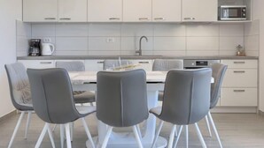 Una cocina moderna con armarios blancos, microondas integrado y un comedor con sillas grises y una mesa blanca.