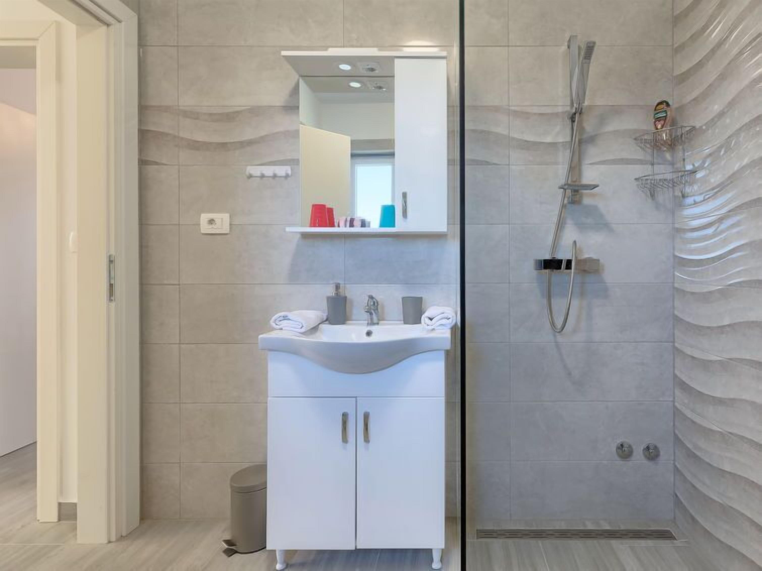 Een moderne badkamer met een witte wastafel, een spiegel en een douche met een gestructureerde wand.