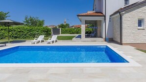 Una piscina con sillones de descanso, un porche cubierto y una pared exterior de piedra.
