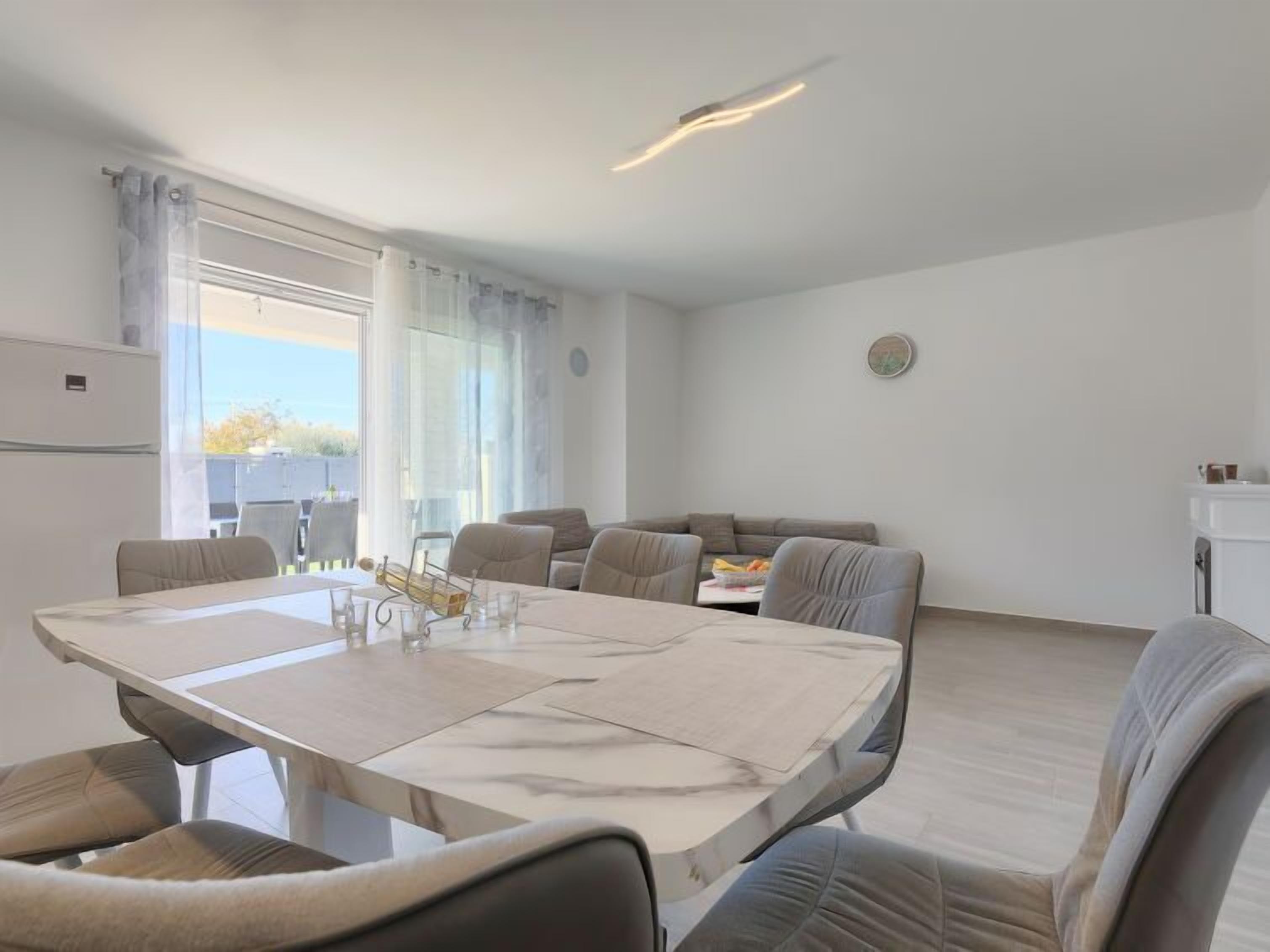 Un salon moderne et bien éclairé, comprenant un coin repas, un ensemble de canapés et un petit espace cuisine.