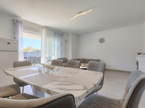 Un salon moderne et bien éclairé, comprenant un coin repas, un ensemble de canapés et un petit espace cuisine.