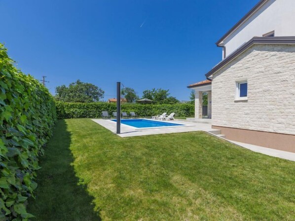 A modern house with a swimming pool, a well-maintained lawn, and a stone facade.