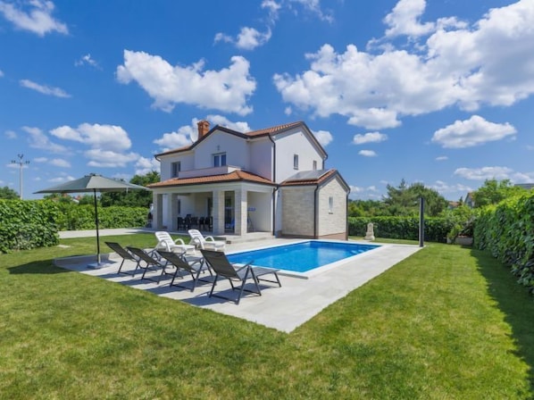 Une maison à deux étages avec une piscine, un patio couvert et une pelouse bien entretenue.