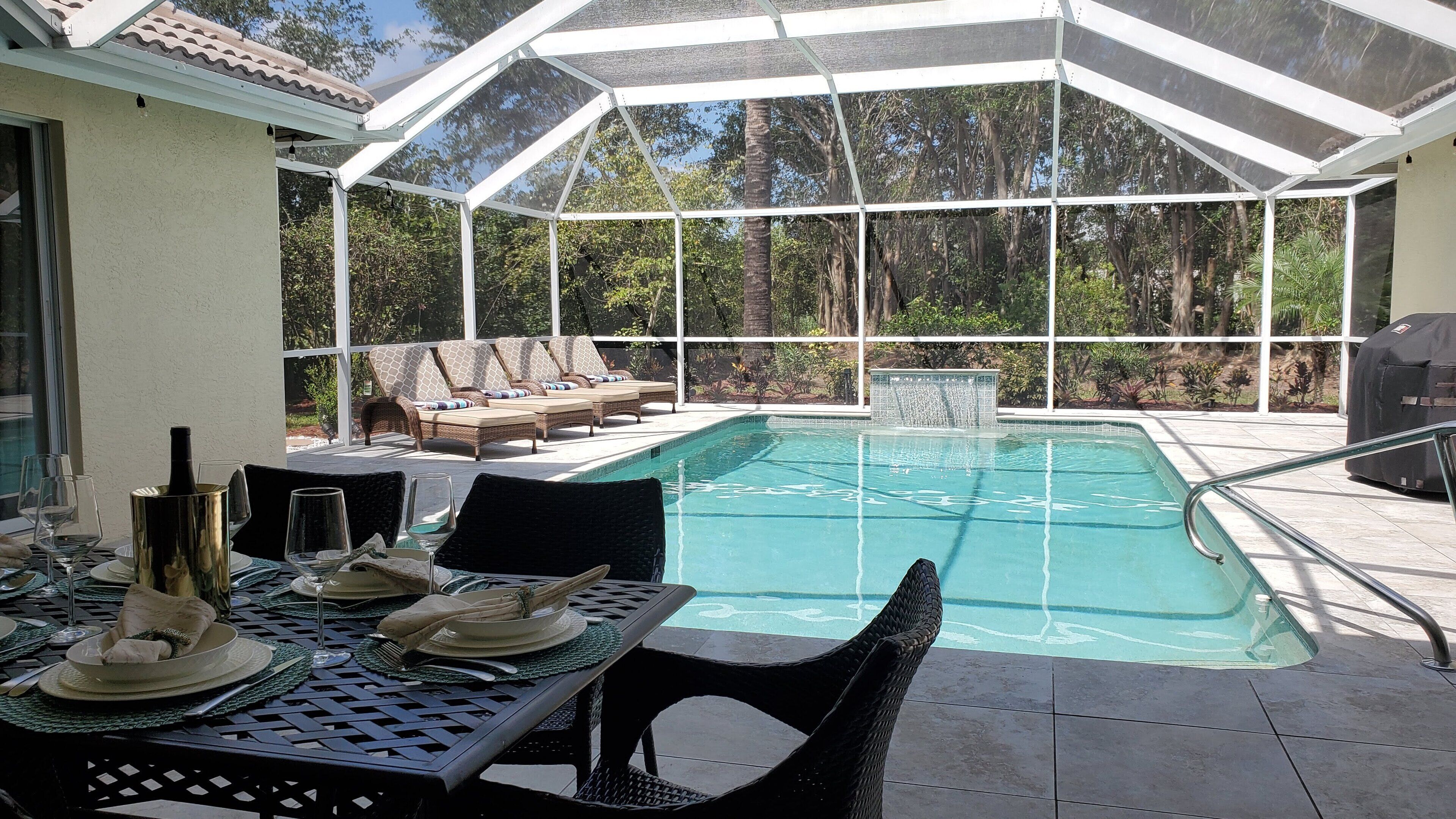 A covered outdoor pool area with lounge chairs and a dining table set for a meal.