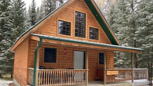 A wooden cabin with a porch, a front door, and a sign that reads "HOMESTEADER." - Homesteader Cabin at Coliseum Mountain Resort (Nordegg)