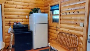 A compact kitchen with wooden walls, a refrigerator, stove, and a bench. - Homesteader Cabin at Coliseum Mountain Resort (Nordegg)